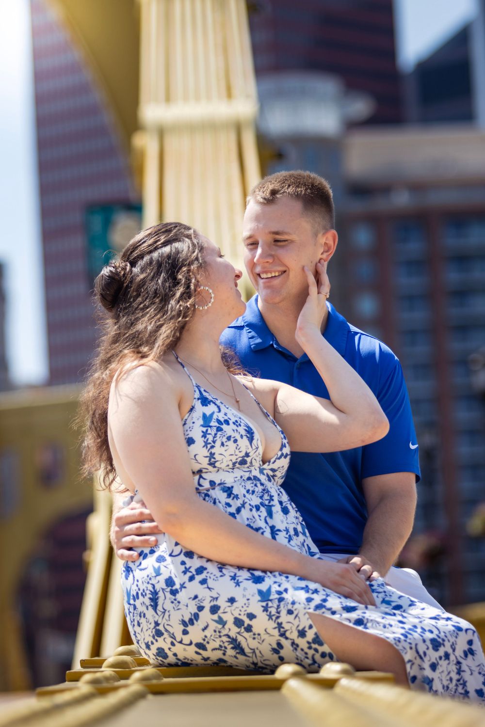 Intimate portrait of couple sitting on golden bridge structure in coordinated outfits.