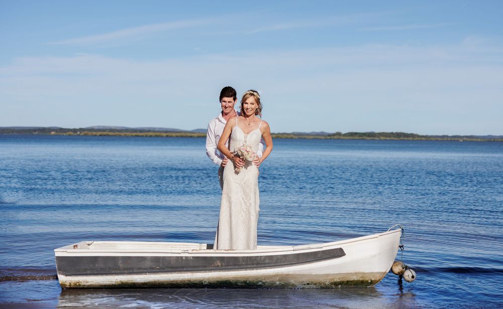 Wedding couple posing near a tranquil lake with boats and blue sky in the background. Redlands