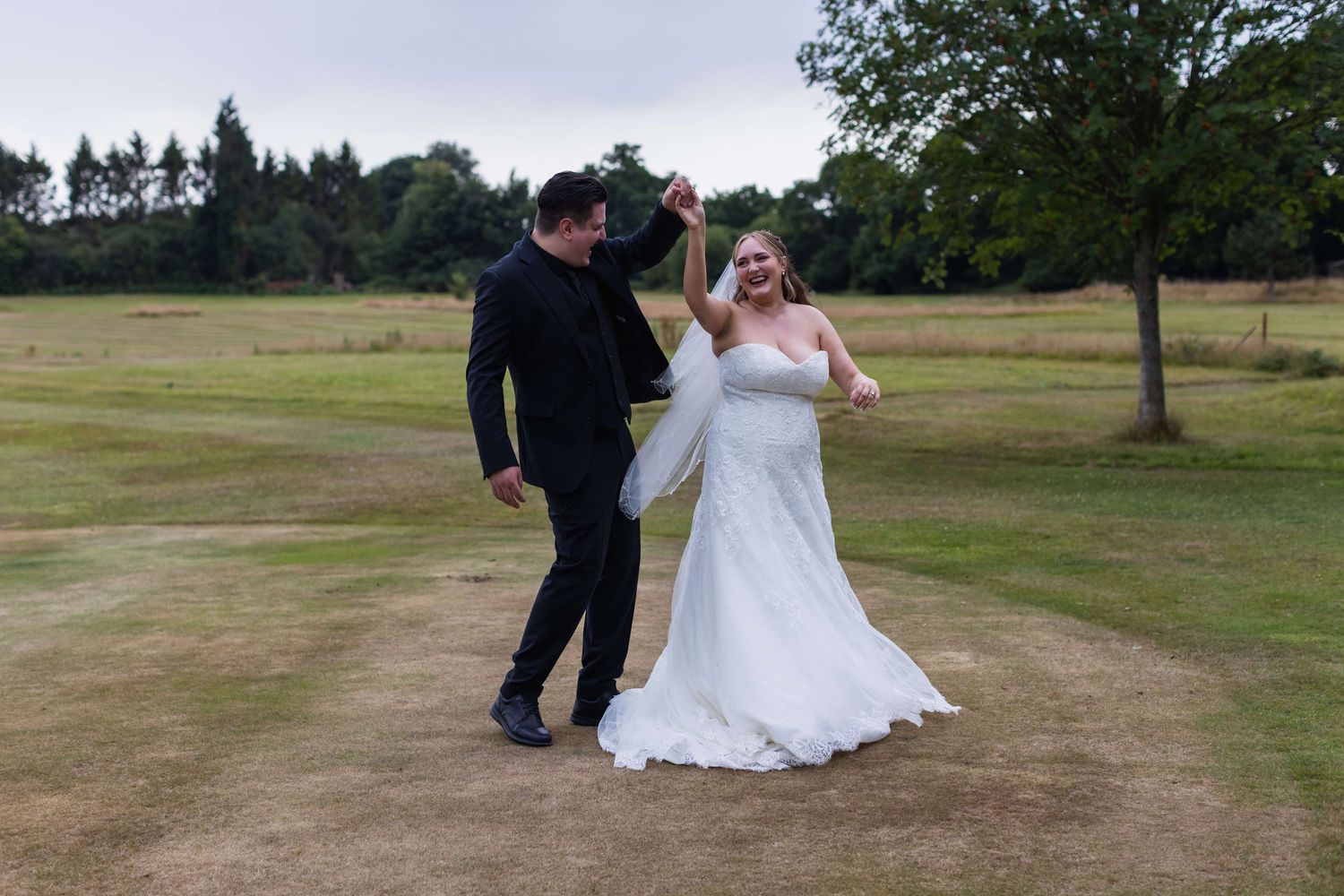 Newly wed couple dancing in a field smiling and laughing at each other