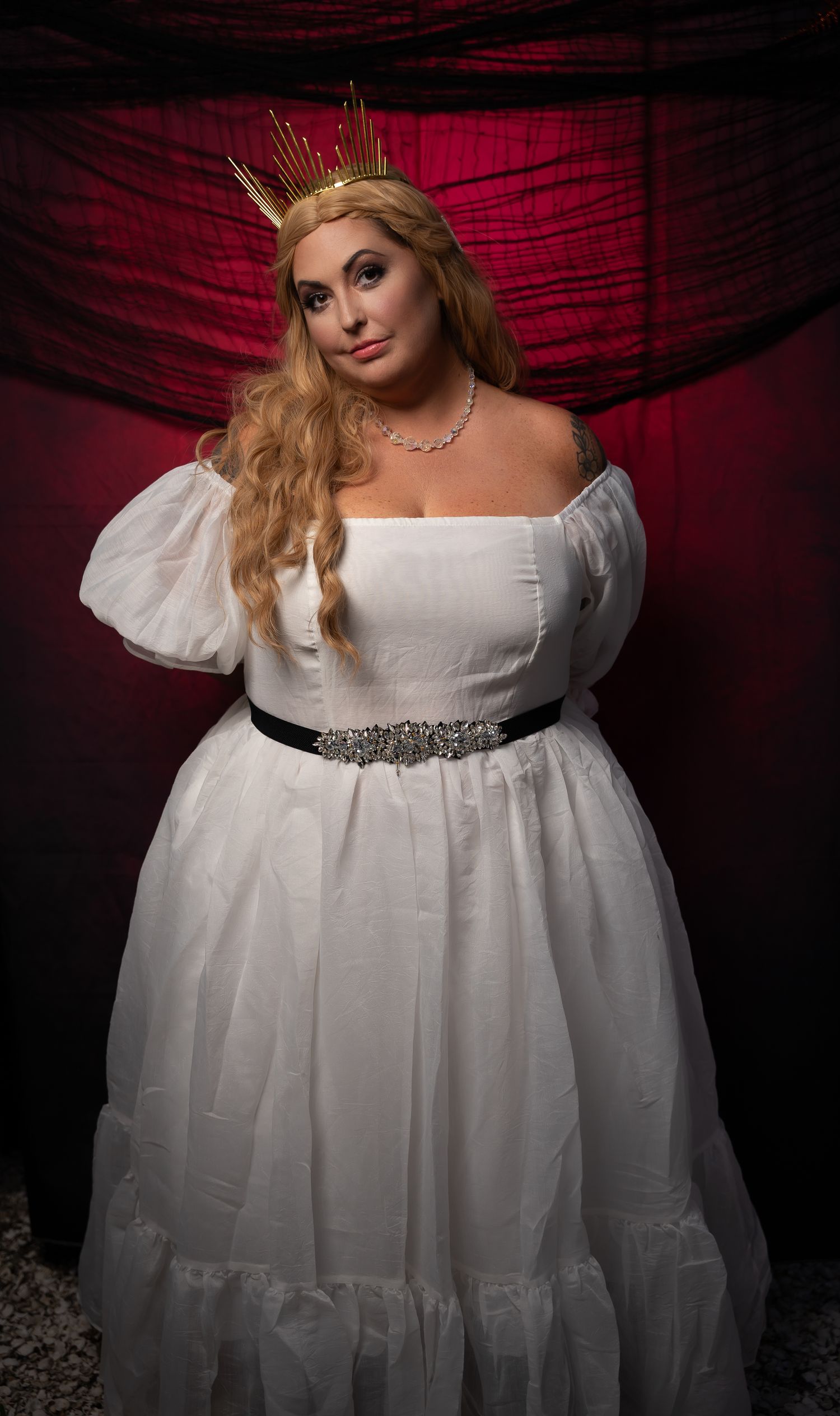 Ethereal portrait against red backdrop featuring a flowing white empire waist gown.