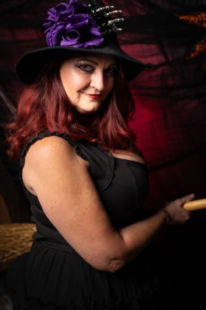Moody portrait featuring black dress and purple hat against dark red backdrop.