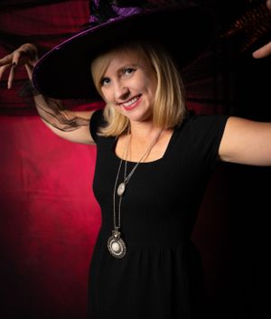 Haunting portrait with a witch hat and pendant necklace against dramatic red lighting.