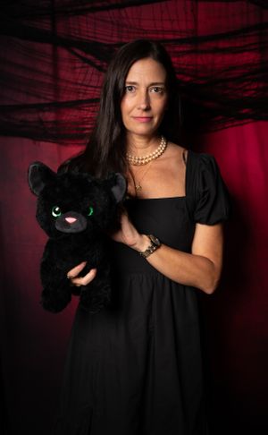 Halloween-themed portrait with black dress, pearl necklace, and plush black cat prop.