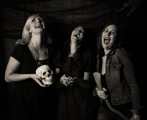 Dramatic black and white group photo with subjects holding skull props and laughing.