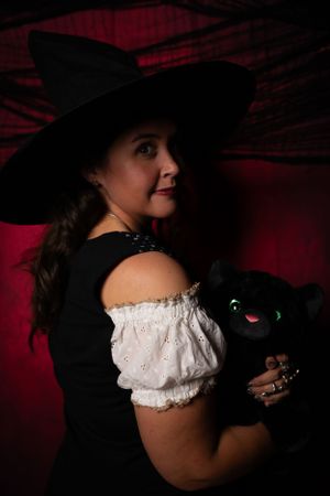 A dark, theatrical portrait with off-shoulder white blouse and black hat.