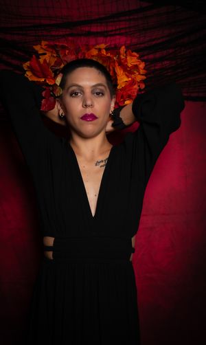 An artistic portrait with orange marigolds and black clothing against red backdrop.