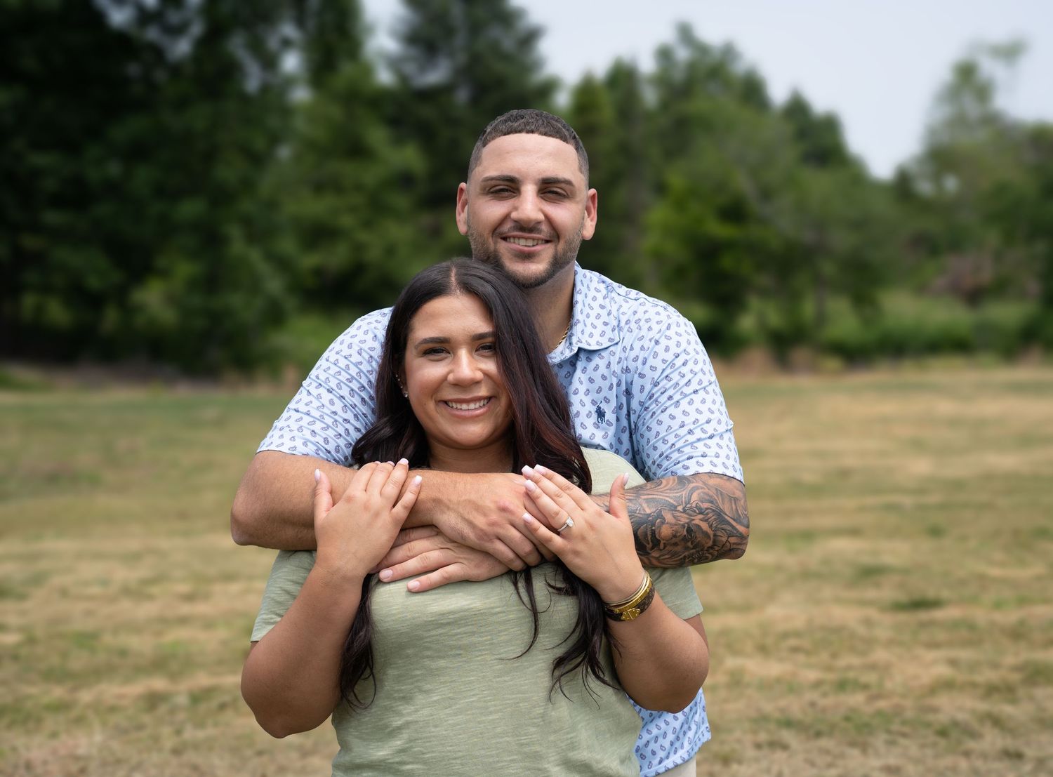 Couple poses together in an outdoor field during a sunny summer day.