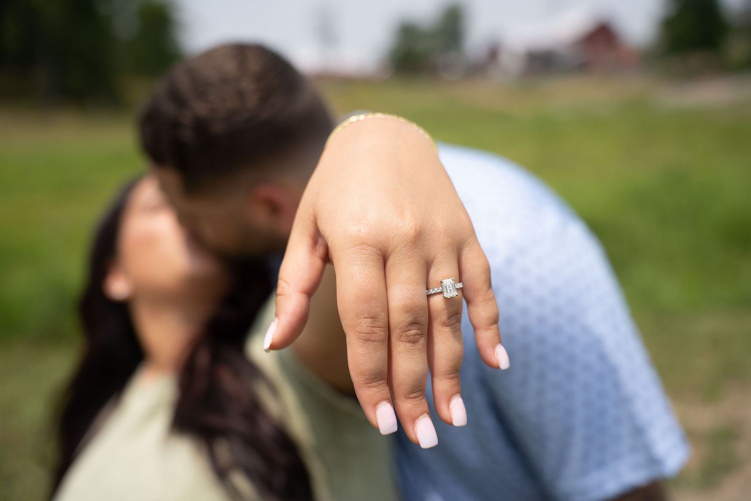 Close-up shot of engagement ring with couple embracing in background.