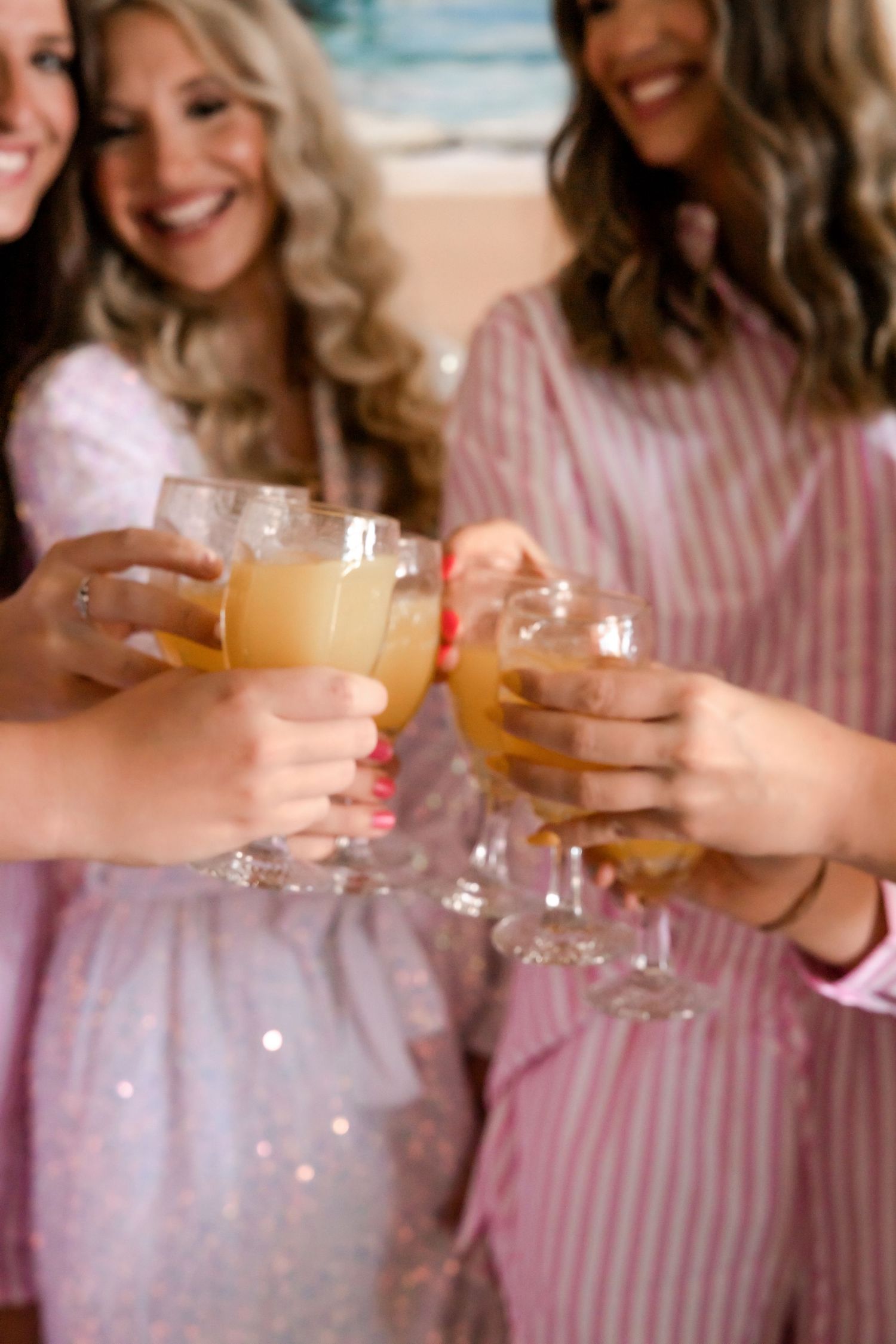 Bridesmaids in pink robes toasting with champagne glasses filled with orange mimosas.