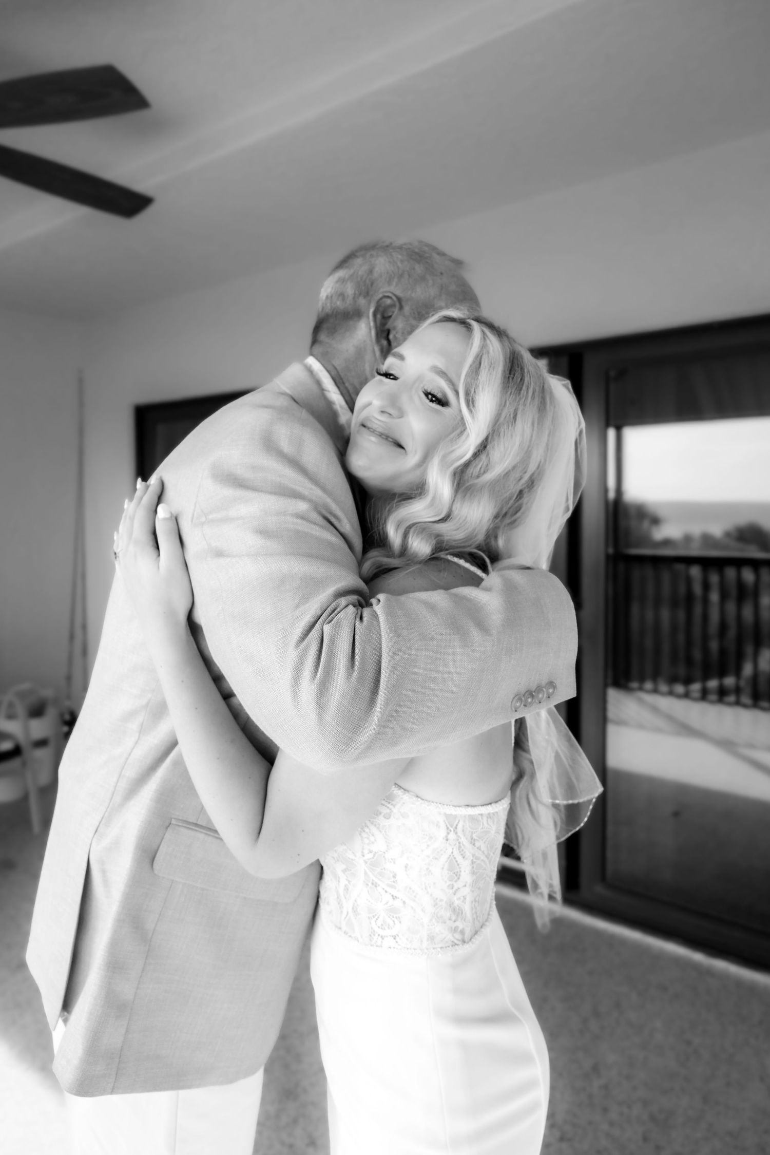 Emotional black and white photo of bride in lace gown sharing a tender hug with her father.
