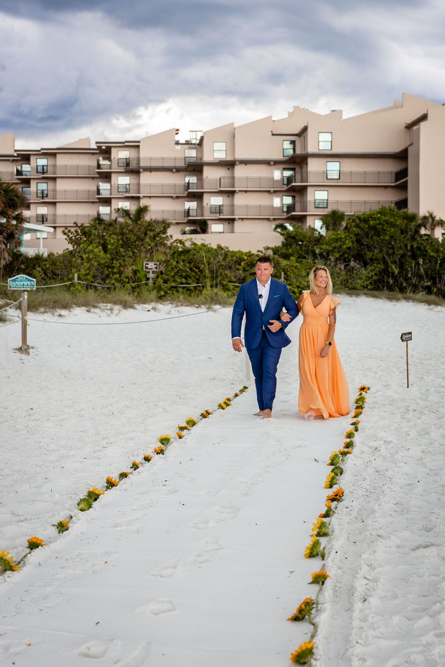 Couple walking hand in hand on a white sand beach path lined with flowers at a Florida resort.