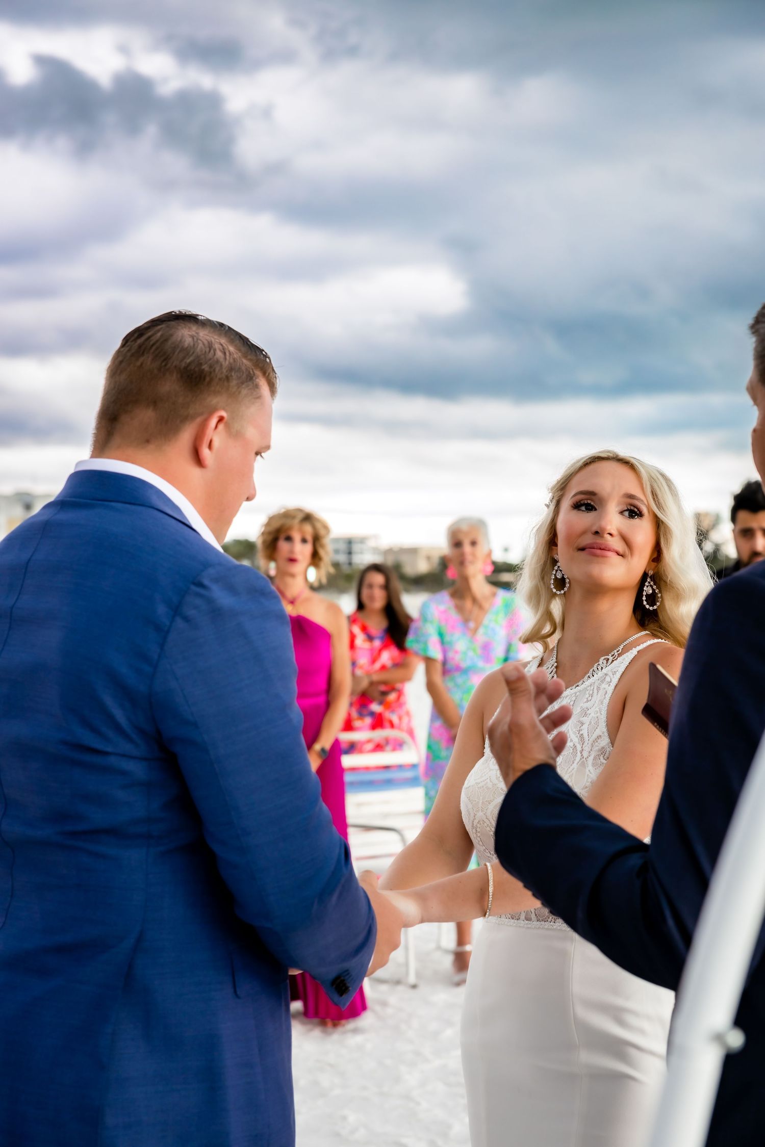 Bride smiles joyfully while holding grooms hands during romantic beach wedding ceremony.