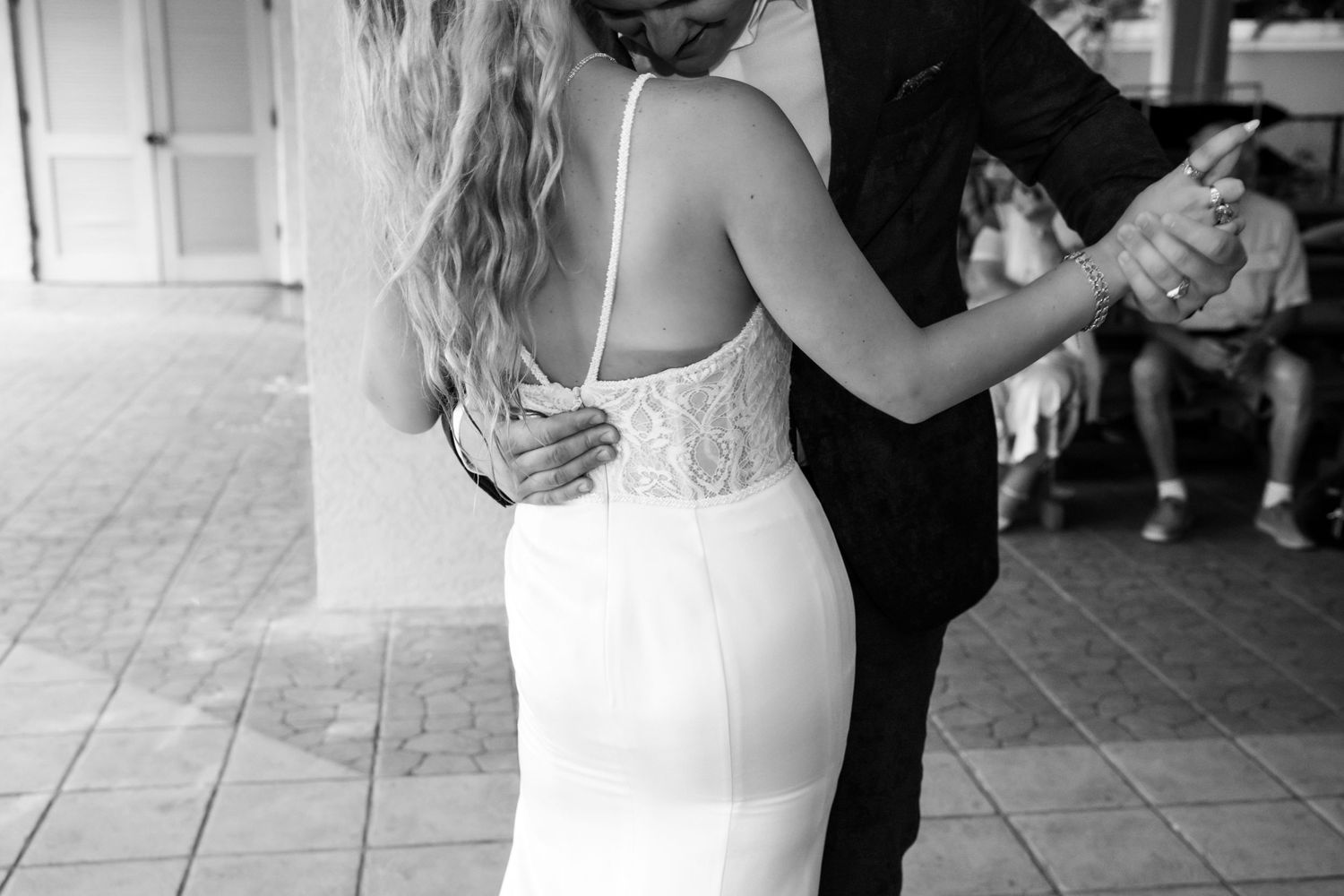 Black and white photo of bride and groom sharing intimate first dance showing back detail of lace wedding gown.