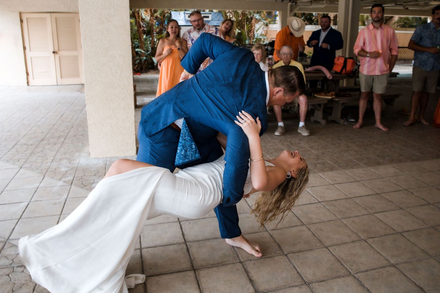 Groom dips bride during wedding reception dance while guests watch in background.