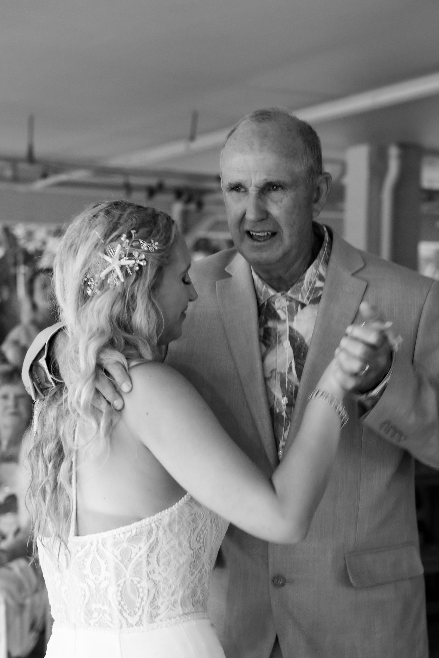 Black and white photo of bride and father sharing emotional dance at wedding reception.