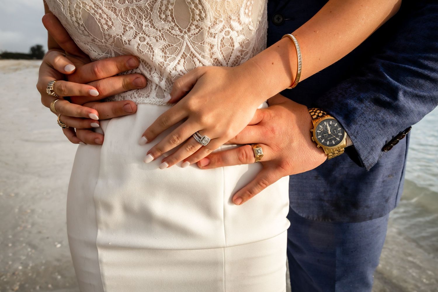 Close-up of bride and groom hands with wedding rings embracing at beach wedding.