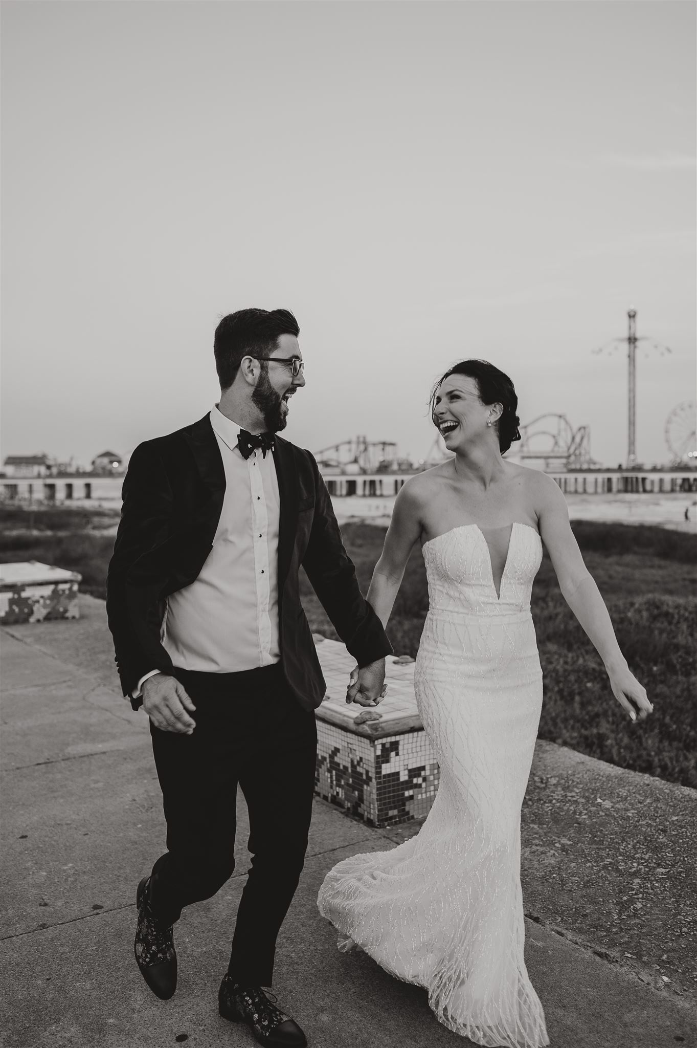 Black and white photo of couple walking and laughing together near pier.