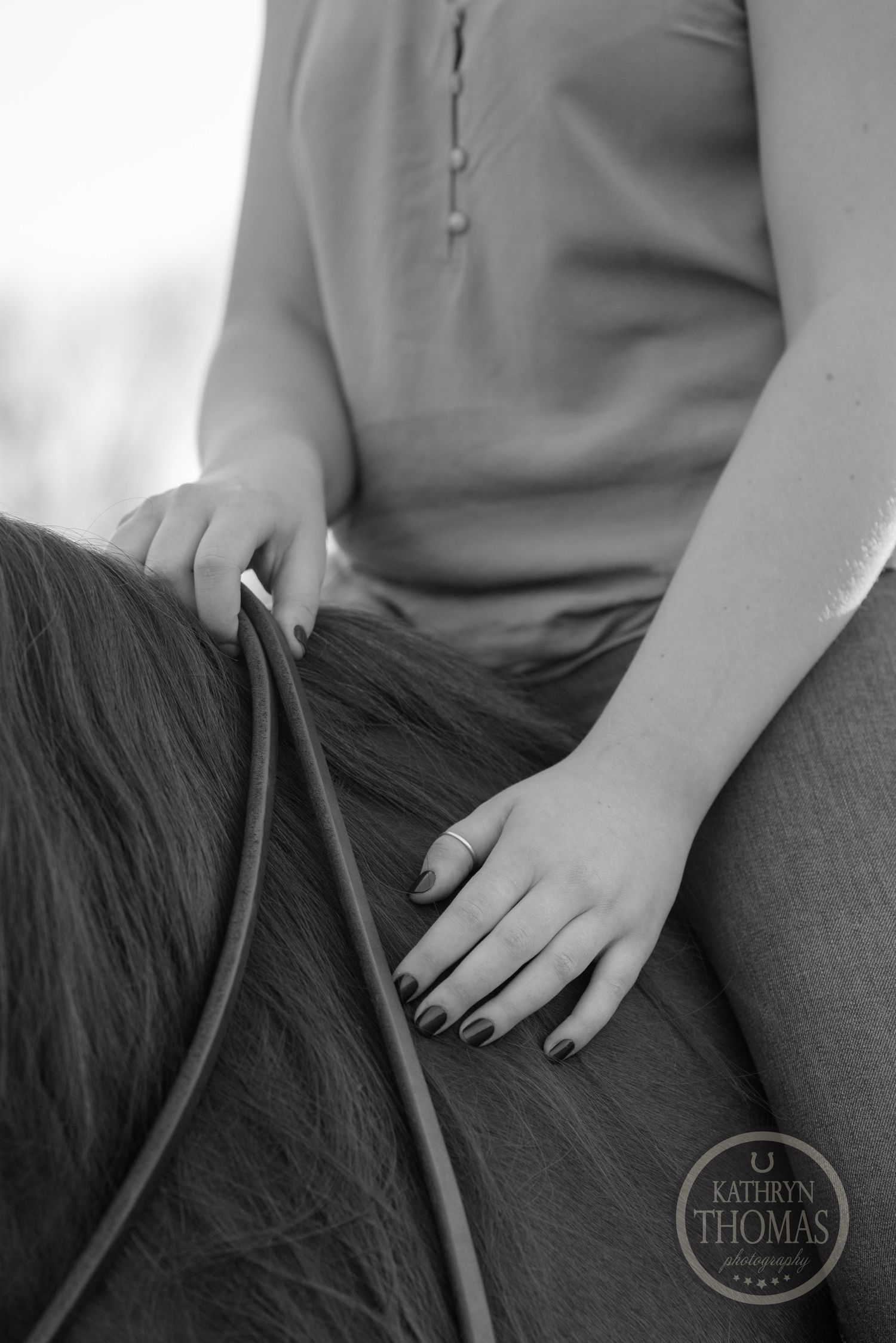 Close-up black and white detail of hands holding horse reins while riding.