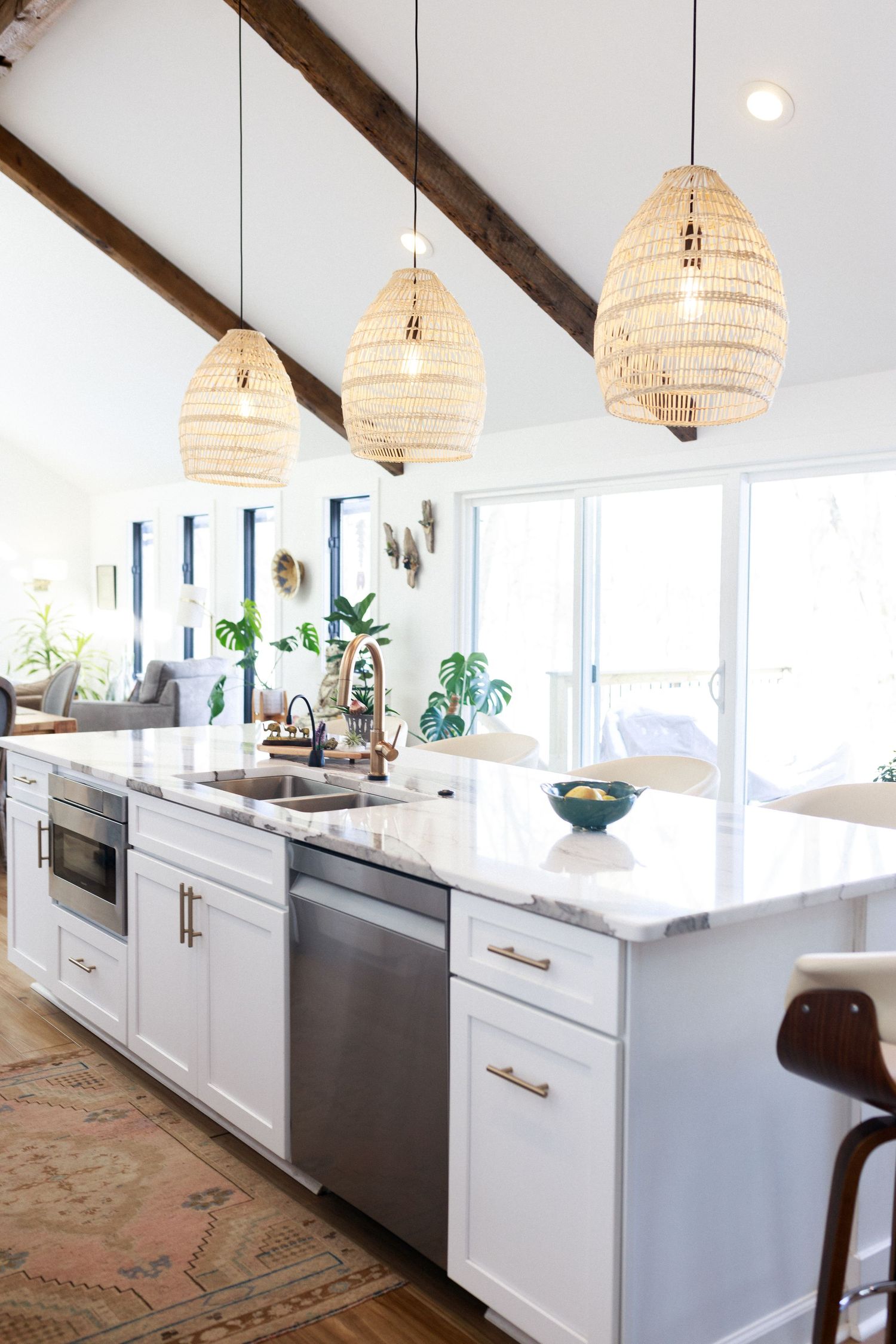 Modern kitchen with white cabinets, marble countertops and woven pendant lights under vaulted ceiling.