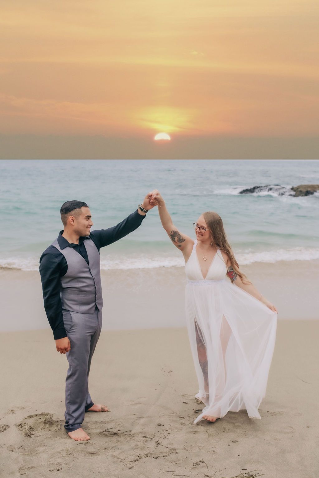 Couple dancing on beach at sunset in formal attire.