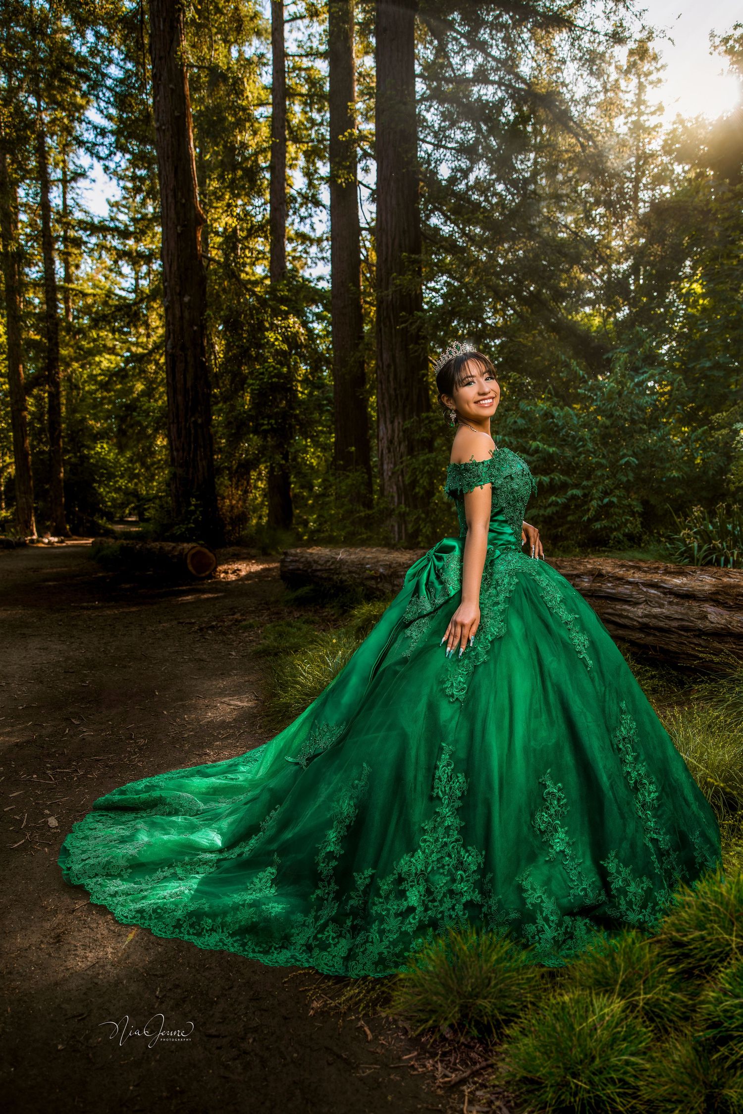 Stunning emerald green ball gown photographed in sunlit forest setting.