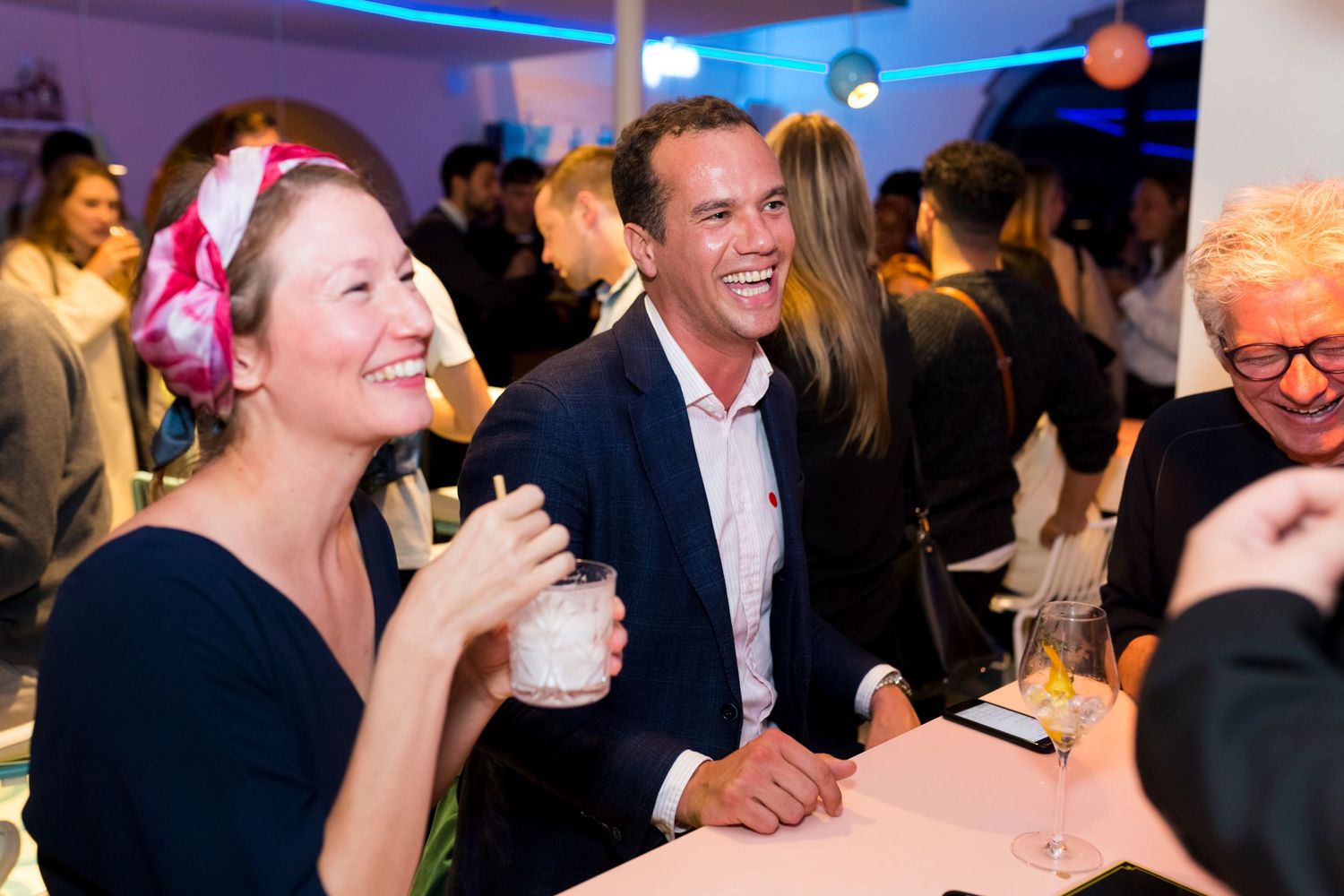 Guests enjoying drinks and conversation at a social networking event with blue lighting.