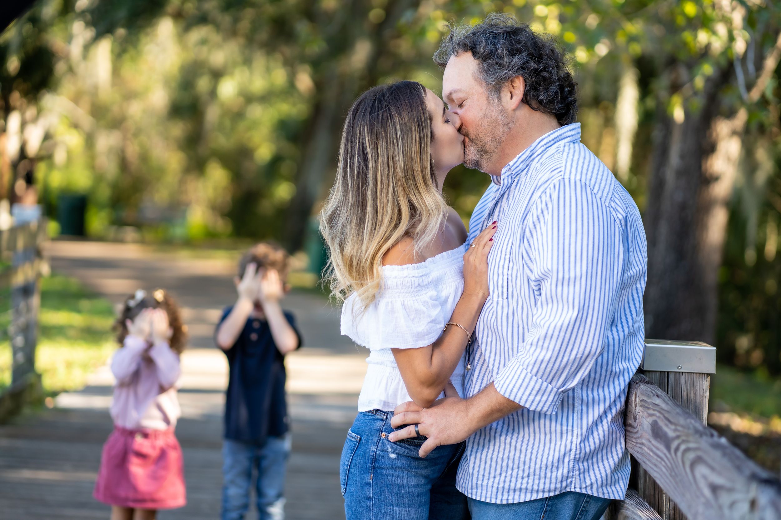 A tender moment captured between a couple on a wooden walkway in a park setting at golden hour.