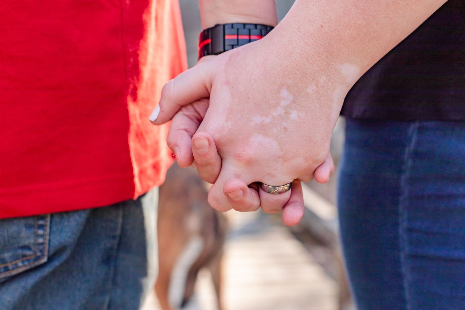 Close-up of two people holding hands outdoors showing rings and casual attire.