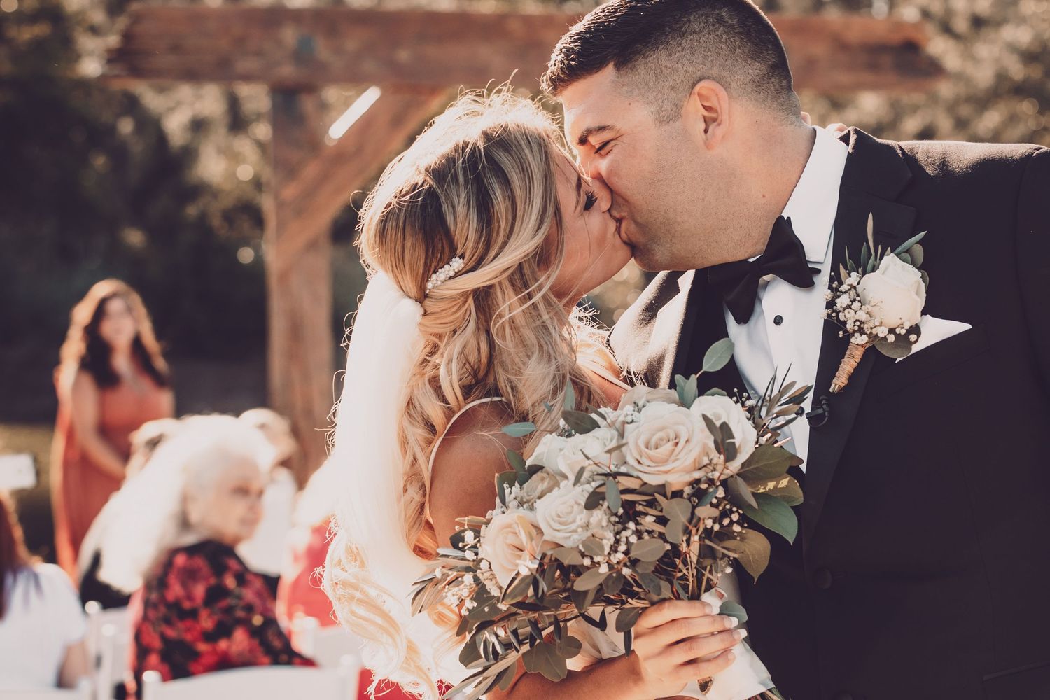 A tender wedding kiss moment with the couple holding a bouquet of flowers.