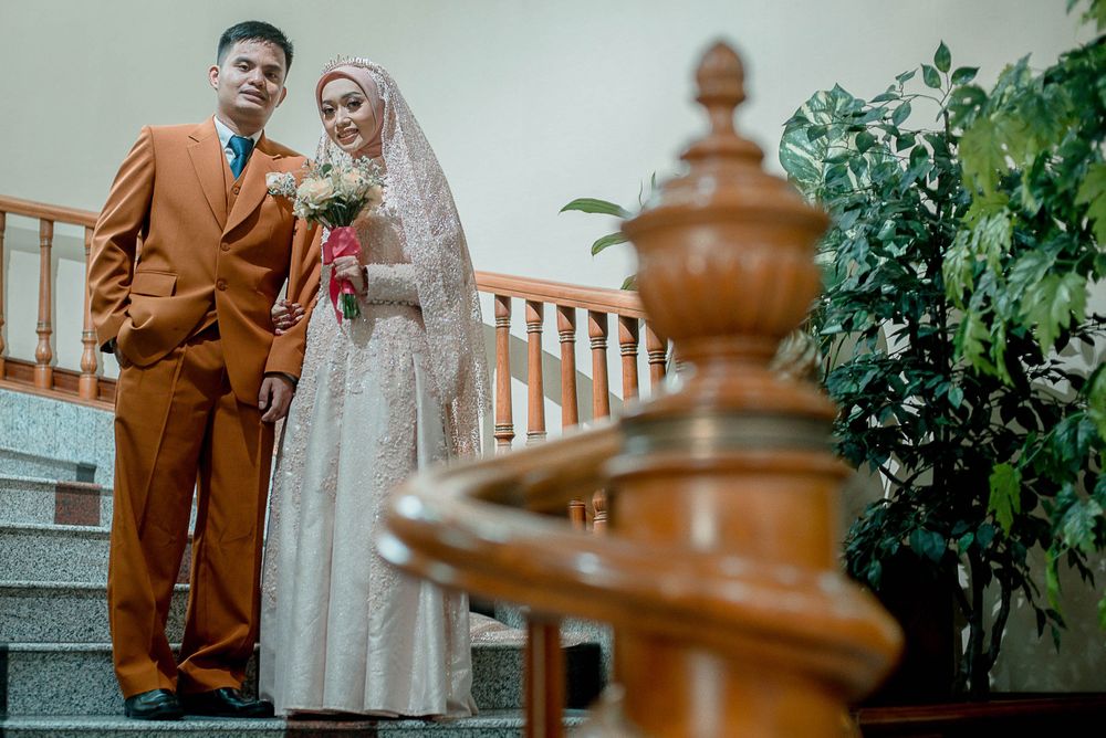 Elegant wedding couple standing on staircase with ornate railing and greenery.