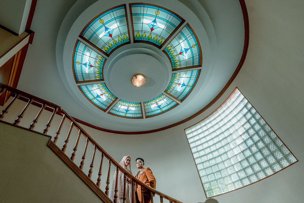 Wedding couple photographed on staircase beneath stunning circular stained glass skylight.