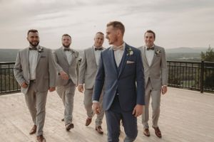Wedding party in stylish grey and navy suits walking together on scenic deck.