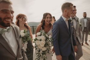 Wedding party walking and laughing together on outdoor deck with white floral bouquets.