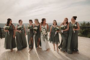 Bridal party in sage green dresses posing on outdoor deck with scenic mountain backdrop.