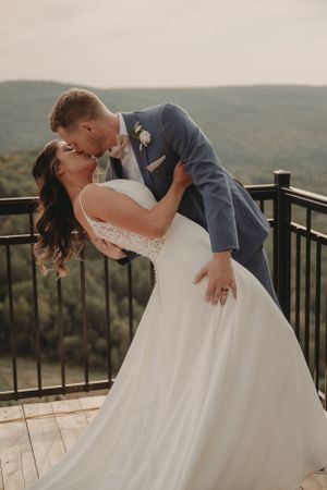 Romantic wedding couple performs classic dip pose on mountain overlook during sunset photoshoot.