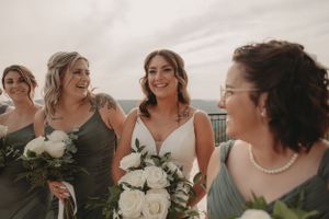 Candid moment of bridesmaids laughing with bride on outdoor balcony.