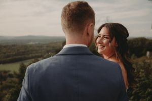 A romantic wedding couple shares an intimate moment while overlooking a scenic mountain landscape at sunset.