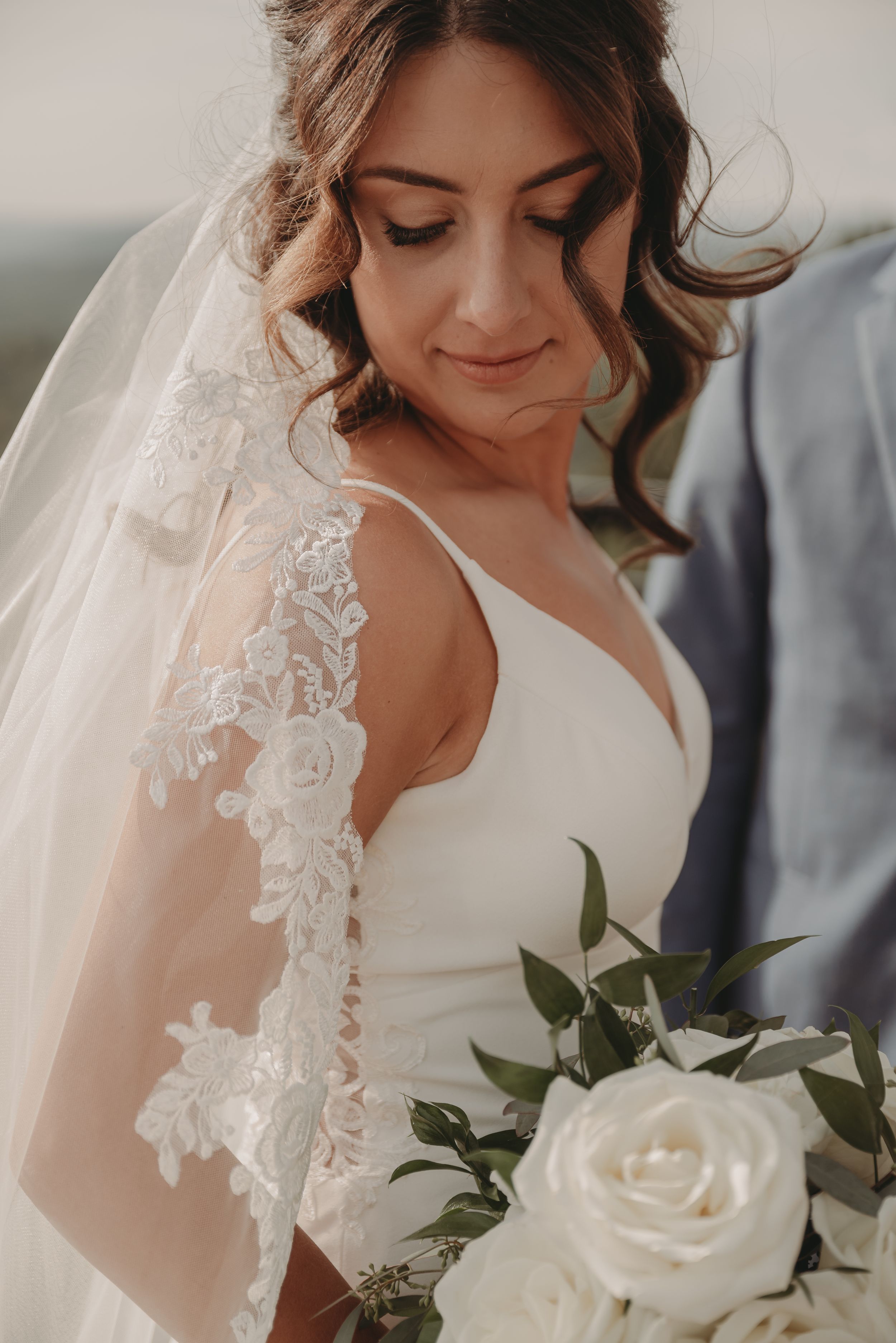 Close-up of a bride in a detailed lace veil holding white roses.