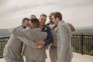 Groomsmen share a celebratory group hug on outdoor wedding venue deck.