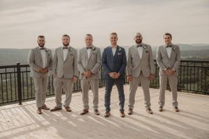 Groomsmen in coordinated grey and navy suits pose together on mountain overlook.