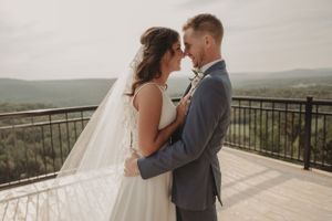 Romantic wedding couple embraces on scenic mountain overlook deck at sunset.