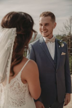Happy newlyweds share a joyful first look moment on an outdoor deck with mountain views.