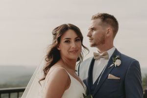 A wedding couple poses together on a scenic overlook deck with mountains in the background.