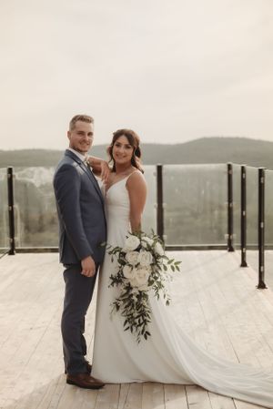 Elegant wedding portrait on deck featuring white cascading bouquet and mountain vista.