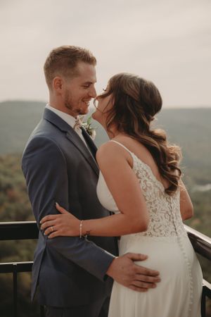 Happy newlyweds embrace on a deck overlooking rolling hills during their wedding celebration.
