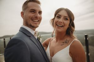 A joyful wedding couple sharing a candid moment on an outdoor deck with mountain views in the background.