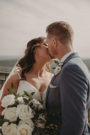 An intimate wedding kiss captured against a mountain landscape backdrop.