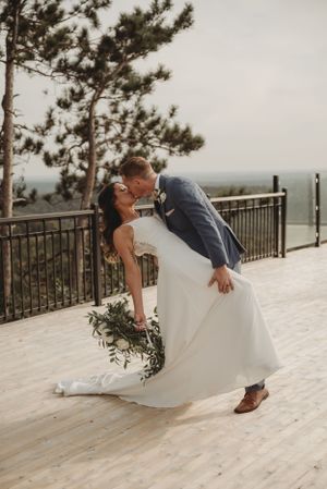 A dramatic wedding photo with the couple sharing a romantic dip kiss on a wooden deck.