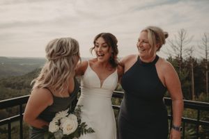 Bride shares joyful moment with two wedding guests on outdoor deck with mountain views.