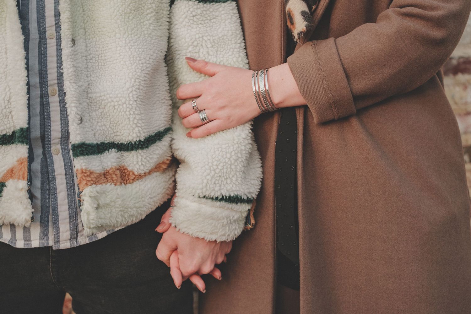 Close up of two people holding hands while wearing winter coats.